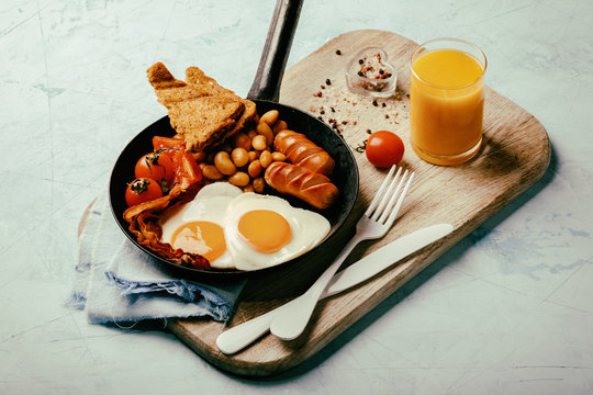 English Breakfast in a skillet. Eggs in the Heart shape. Valentine's Day. Festive Food on the Blue Background.Sausages, Bacon, Beans,Orange juice and Coffee.Copy space for Text Toned image