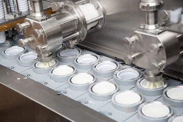 Foto auf Acrylglas Milchprodukte Final Stage Of Production Yogurt-Filling Yogurt Into Plastic Glasses In Modern Dairy