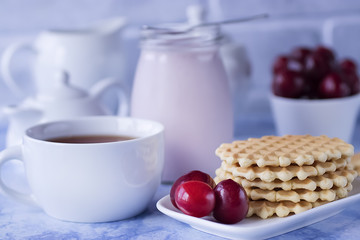 Breakfast. White cup of tea with thin waffles, lemon jam, yogurt and fresh fruit.