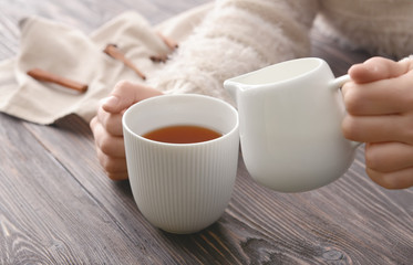 Woman pouring milk into cup of tea on table