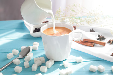 Pouring of milk into cup of tea on wooden table