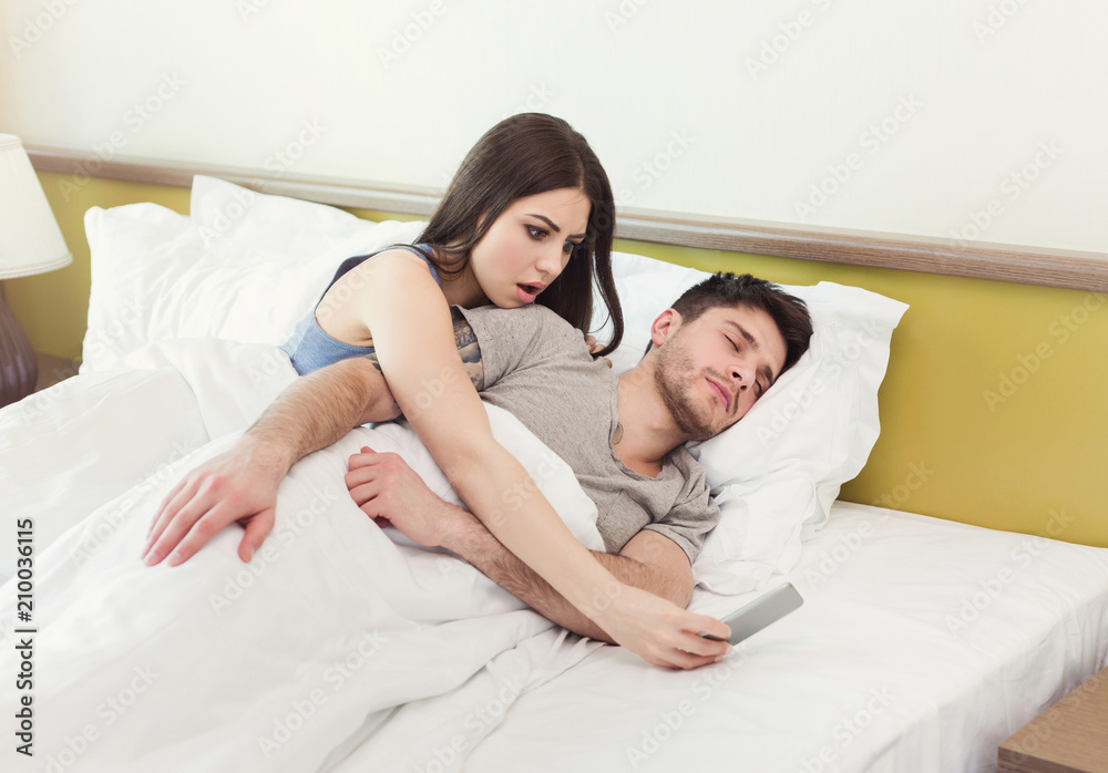 Wall mural jealous wife spying phone of husband while man sleeping