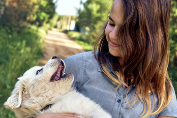Happy teen girl playing with a cute puppy of a pyrenean mountain dog holding it on her hands in summer day outdoors