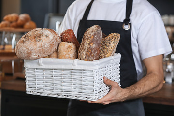 Male baker holding wicker basket with fresh bread in shop