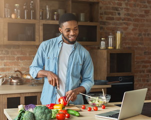 Happy african-american man preparing salad in kitchen