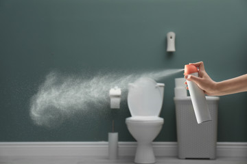 Woman spraying air freshener in bathroom