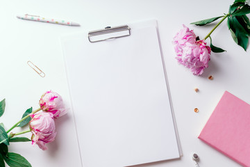 Feminine workspace with empty paper and pink peons on white background with copy space