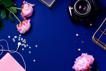 Flat lay composition with peons, earphones, sparkles and vintage photo camera on blue background. Top view, colorful workspace concept