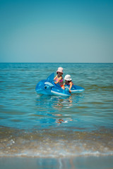 two little girls are swimming on pumped dolphin in the sea in summer