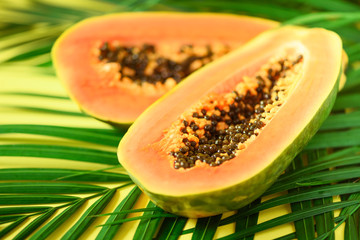 Exotic papaya fruit over tropical green palm leaves on yellow background. Copy space. Pop art design, creative summer concept. Raw vegan food.
