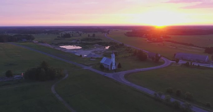 Amazing aerial view of beautiful sunset over the small country town. Green fields and tall trees. Nature / town landscape.