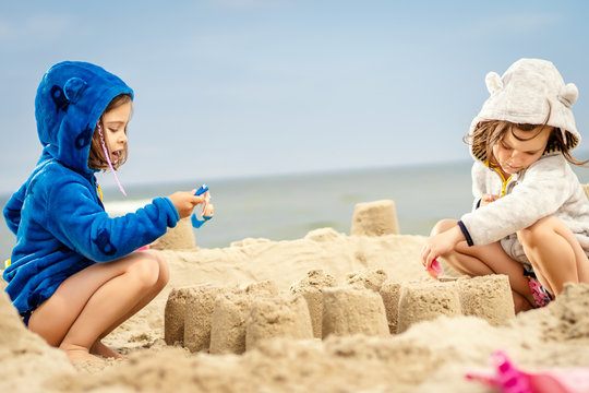 two little girls play with dolls in a sand castle on the beach in summer
