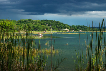View on the village with dock along the lake shore with dark blue cloudscape, El Remate, Péten, Guatemala