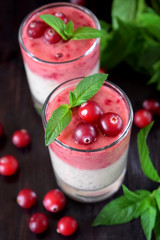 Two layered smoothie in glasses surrounded by cranberries and mint against the dark background