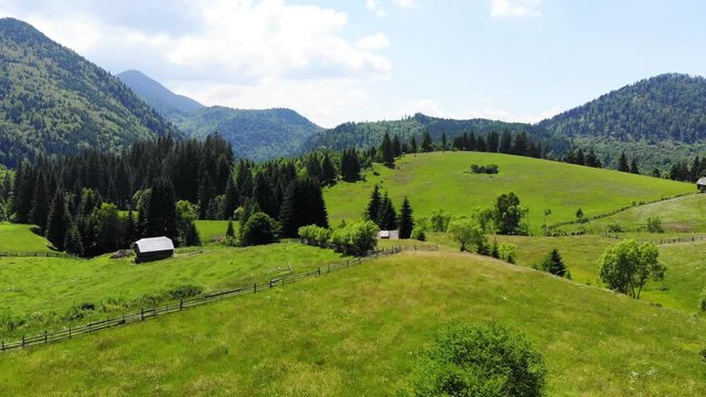 Panoramic view of idyllic mountain scenery with fresh green meadows in bloom on a beautiful sunny day in springtime. Aerial 4K view. Low air flight over mountain rural farm and meadow at sunny day