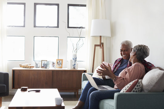 Senior Couple Sitting On Sofa At Home Using Laptop To Shop Online