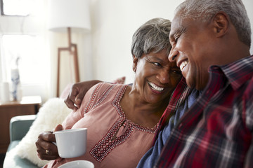 Loving Senior Couple Sitting On Sofa At Home Relaxing With Hot Drink - Powered by Adobe