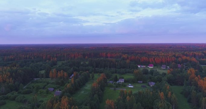 Amazing aerial view of beautiful sunset over the small country town. Green fields and tall trees. Nature / town landscape.