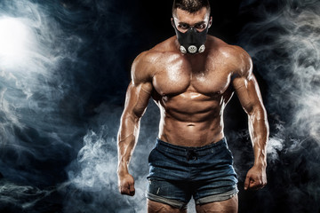 Muscular young fitness sports man in training mask. Workout with dumbbell in fitness gym. Copy space for fitness nutrition ads.