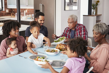 Multi Generation Family Enjoying Meal Around Table At Home