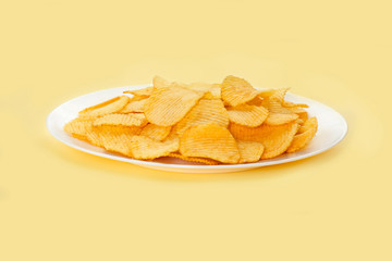Potato chips in a white plate isolated on bright yellow background . Fast food. Side view