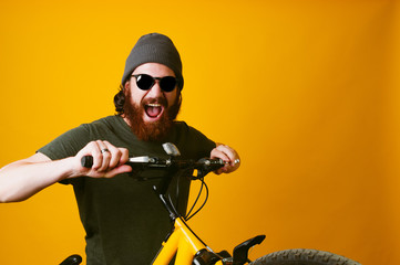 Fototapeta na wymiar Close up portrait of amazing bearded hipster man riding a bicycle in studio over yellow background