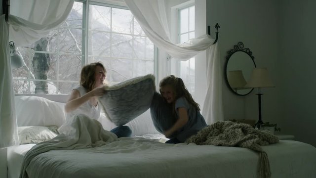 Slow motion of mother and daughter having pillow fight in bed / Pleasant Grove, Utah, United States