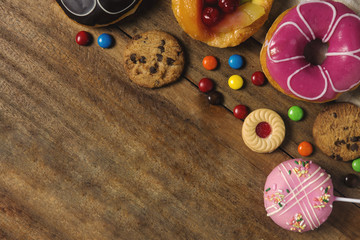 Round donuts, cookies, and fruitcake, flat lay dessert on wooden table decorate with candy