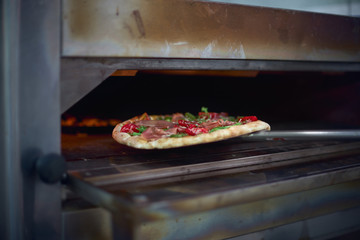 Cook putting Italian pizza to bake in oven