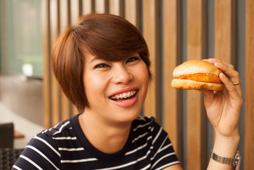 Asian women is biting a burger,women enjoy eating with her burger in hands,delicious burger,asian women are hungry,Orthodontics women enjoy eating burger,holding burger