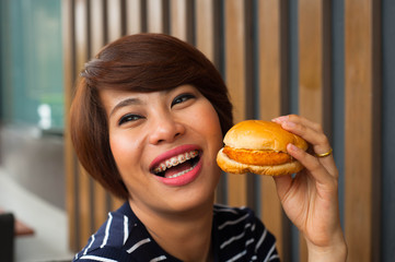 Asian women smile with her burger,Asian women is biting a burger,women enjoy eating with her burger in hands,delicious burger,asian women are hungry,Orthodontics women enjoy eating burger