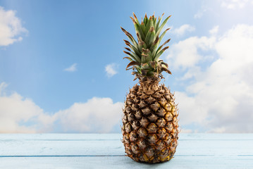 organic pineapple fruit on a wooden table against a blue sky with clouds, copy space