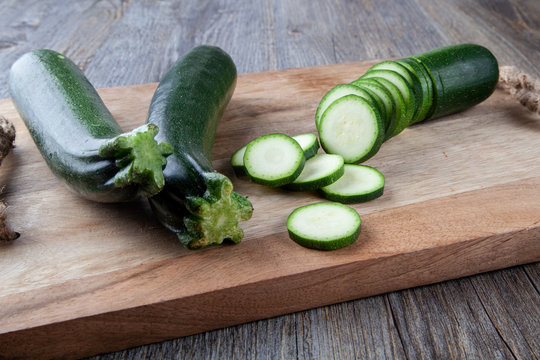 Two Courgettes on a wooden chopping board and another sliced courgette