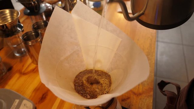 Barista pours boiling water, making dripping coffee servicing an order in cafe