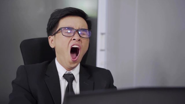 tired young businessman using laptop and yawning 