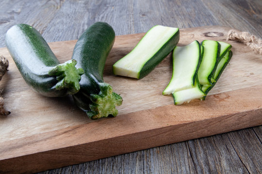 Two Courgettes on a wooden chopping board and another julienne courgette