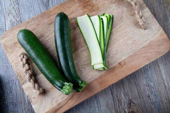Overhead view ofTwo Courgettes on a wooden chopping board and another julienne courgette