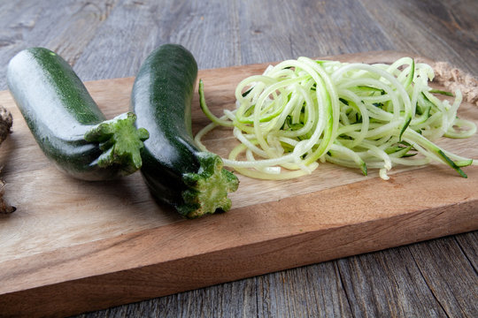 Two Courgettes on a wooden chopping board with a pile of courgette spaghetti
