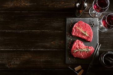 two pieces of fresh meat prepared for frying and wine with glasses on a wooden table
