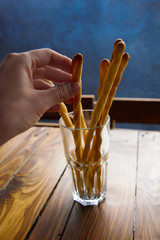 the hand reaches for bread sticks with sesame seeds in rustic decor. grissini in the glass
