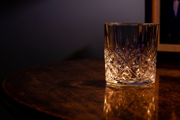 An empty crystal glass resting on on a table with a dark wood grain
