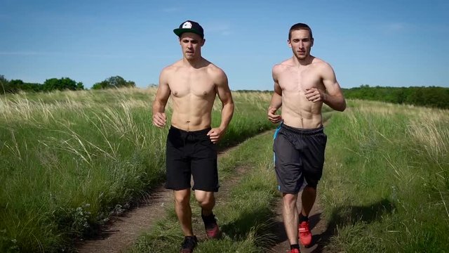 Two shirtless muscular men exer ising in nature in summertime.