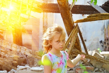 The sad orphan girl was left homeless and points to the ruins of the ruined building as a result of...