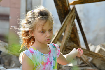 The sad orphan girl was left homeless and points to the ruins of the ruined building as a result of...