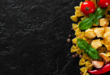 food background. Ingredients for cooking Italian pasta - farfalle pasta, red chili peppers, cherry tomato, basil, black pepper, garlic, parmesan cheese on dark background with copy space. top view
