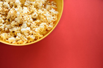 Tasty caramel popcorn in a yellow plate on a red background, top view with copy space