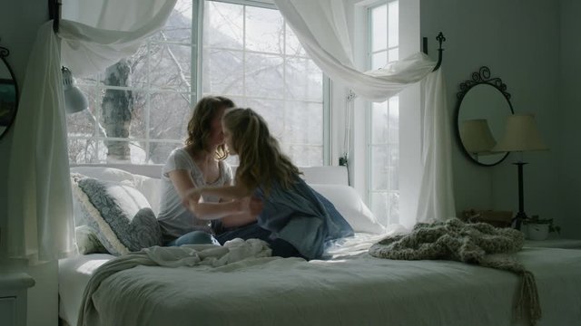 Slow motion of mother and daughter talking in bed then hugging bed near bay window / Pleasant Grove, Utah, United States