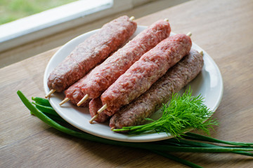 Raw lulya kebab from meat on a white plate with with dill and green onions.