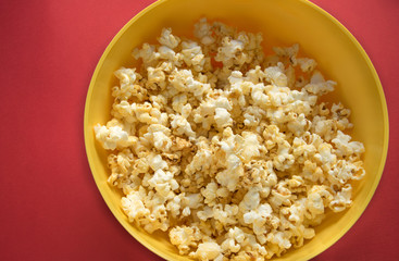 Tasty caramel popcorn in a yellow plate on a red background, top view 