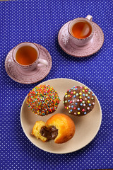 Baking with tea and chocolate on the table.  Two cups of tea with cupcakes and chocolate with a multicolored powder on the table.